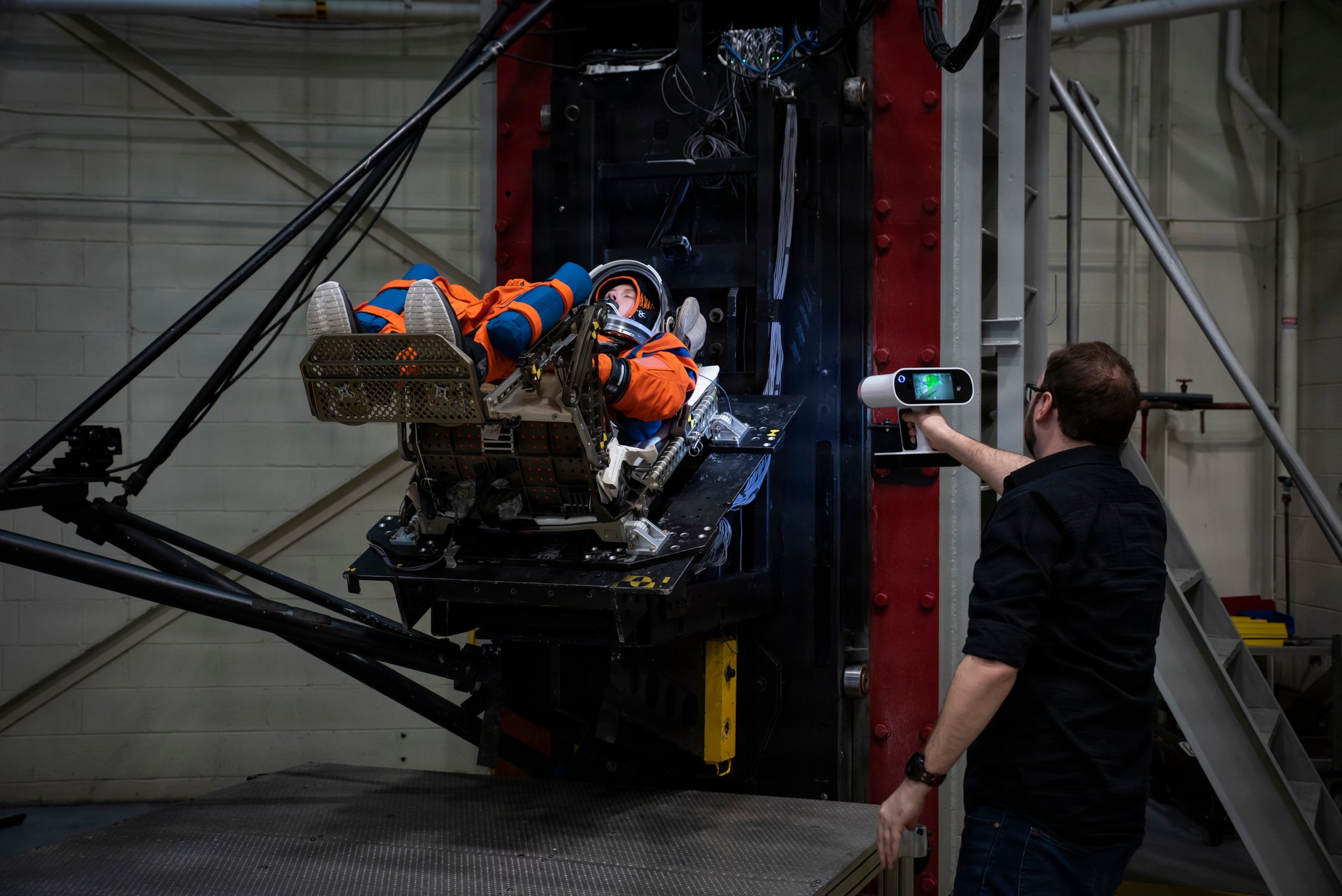 An engineer scans a suited test subject strapped into a seat on a test rig