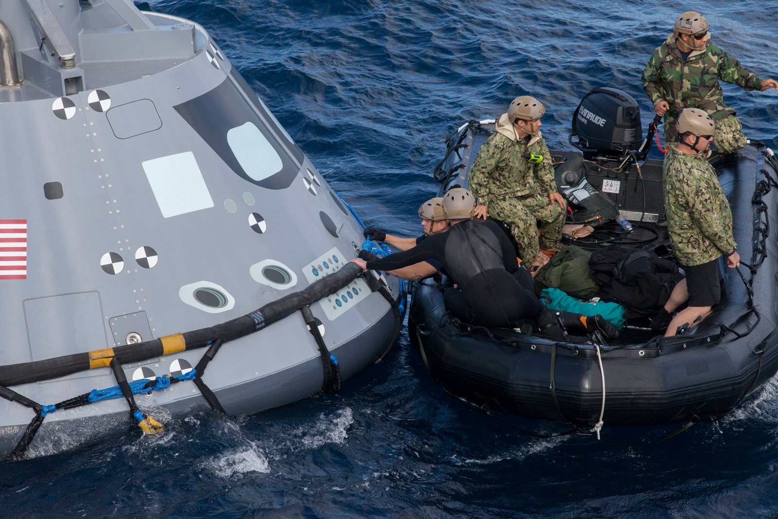 Recovery team members in an inflatable boat alongside an Orion capsule at sea