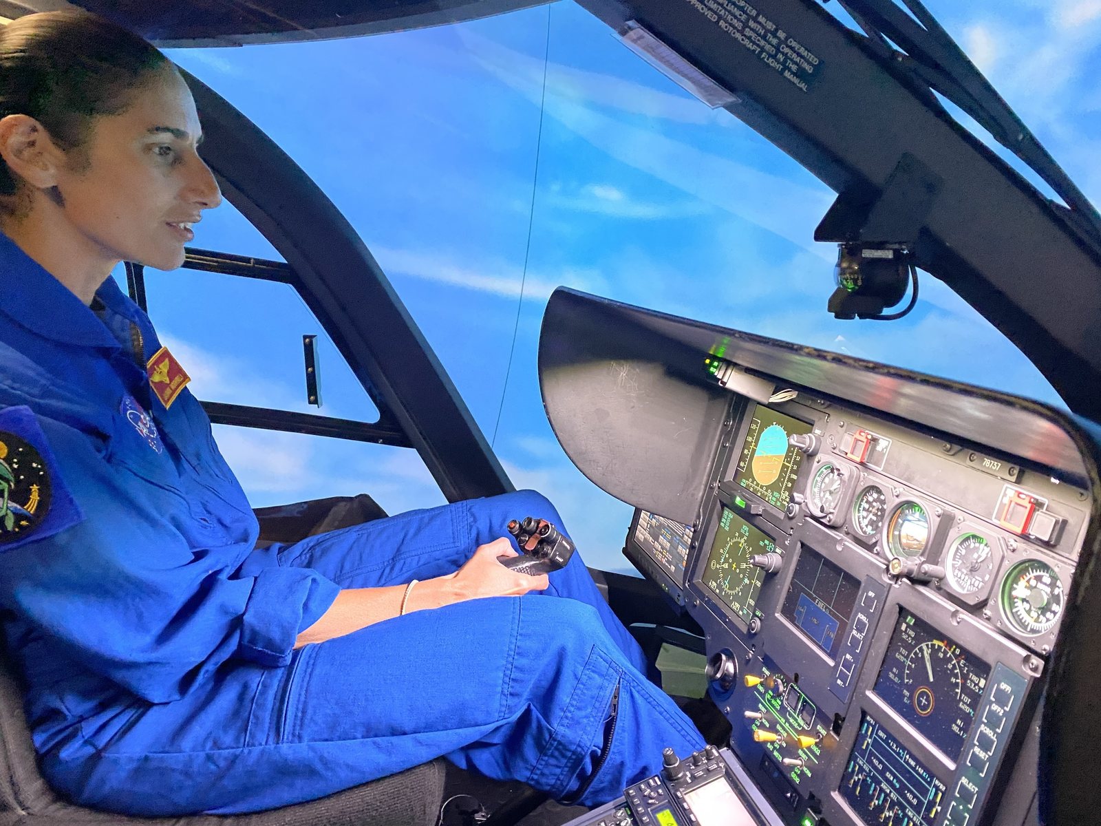 An astronaut in a blue flight suit at the controls of a flight simulator